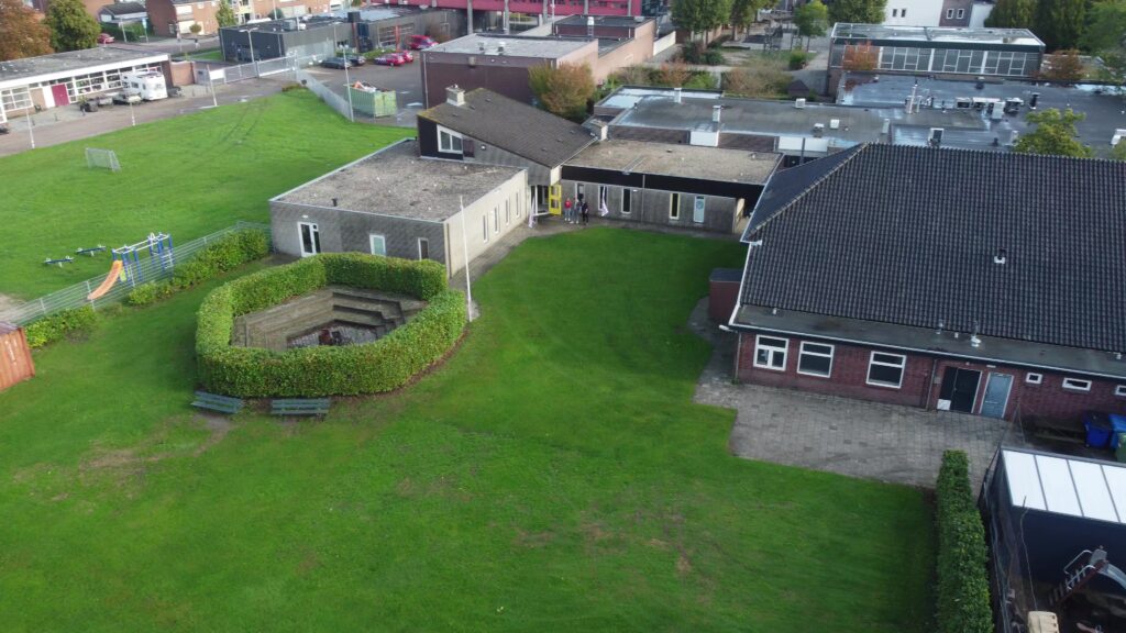 Luchtfoto met overzicht van het gebouw, veld en kampvuurkuil.